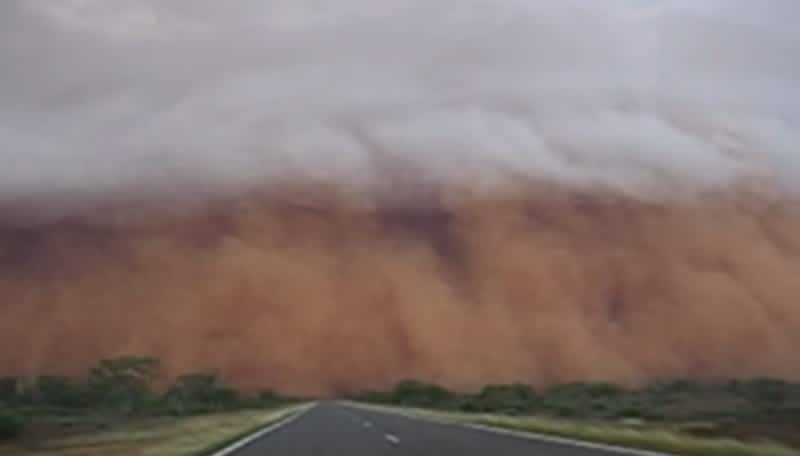 Massive real-life dust storm engulfing cars on a highway, resembling a Mad Max scene
